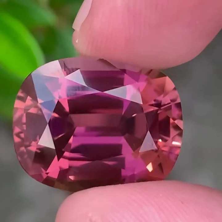 23.35 ct fuchsia pink tourmaline, cushion fine step cut, held between the fingers