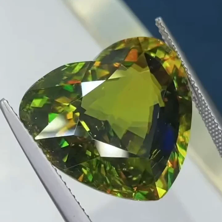 26.85 ct green sphene, heart fine step cut, held in tweezers