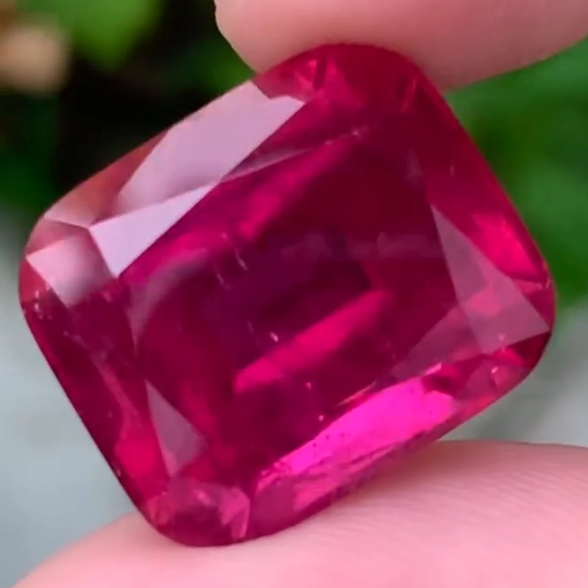 A cushion cut rubellite tourmaline in deep raspberry red held between two fingers