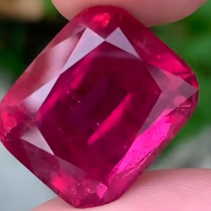 26.37 ct rubellite tourmaline, cushion fine step cut, held between the fingers