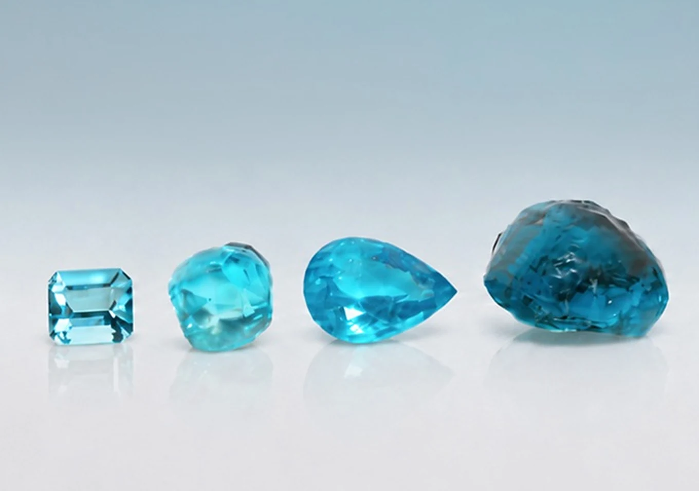 Four Ethiopian copper-bearing tourmalines in vivid blue: an emerald cut, a rough-cut cushion, a pear shape and a large rough stone