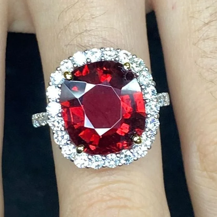 A cushion cut red gemstone ring surrounded by a halo of round diamonds, worn on a hand