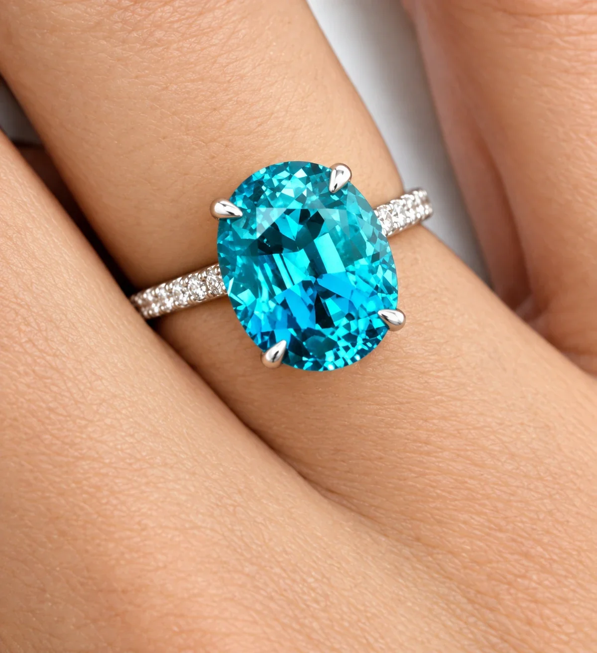 A white gold ring with a large vivid blue oval gemstone and a diamond set band, worn on a hand