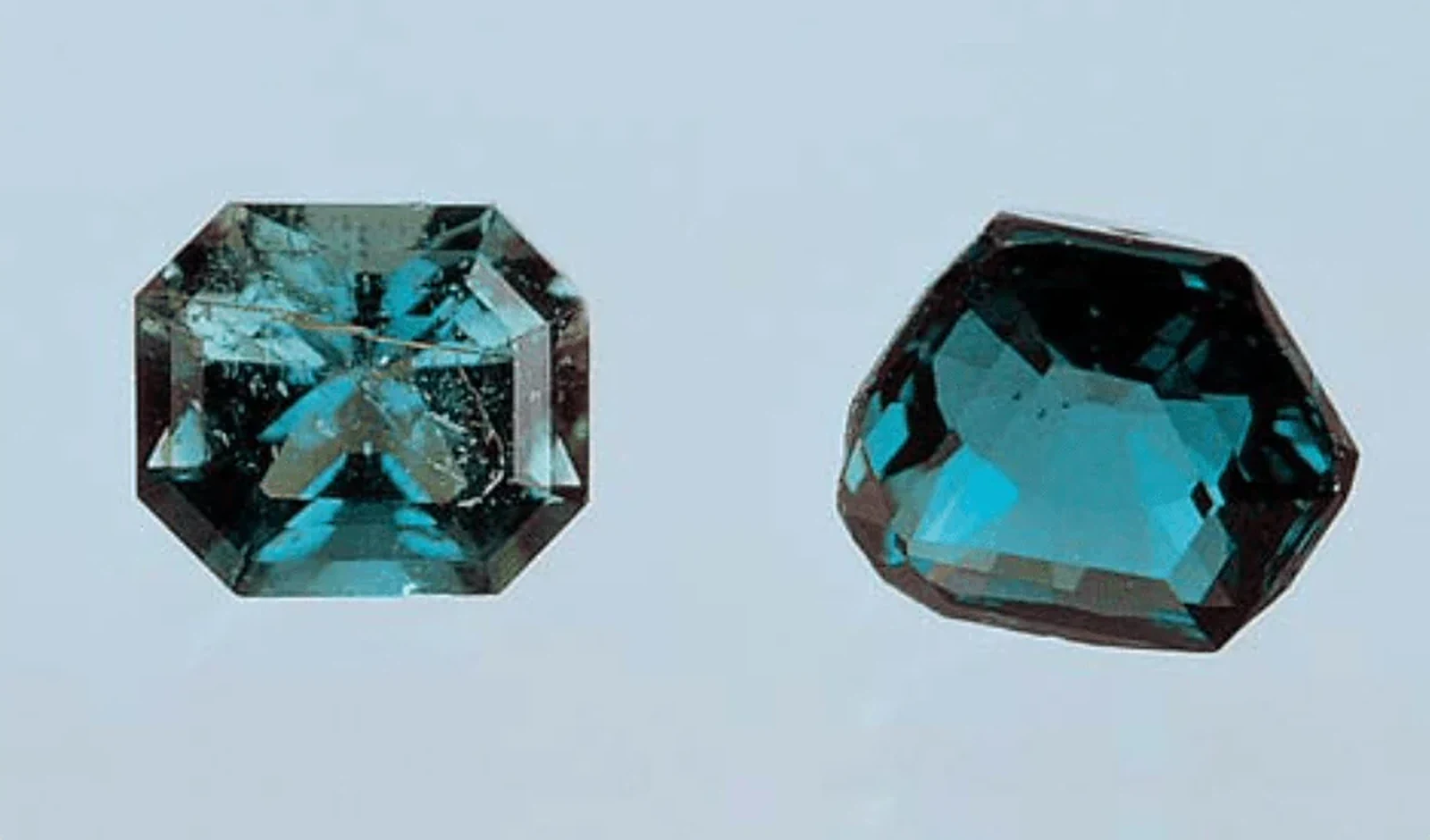 Two faceted blue green serendibites, one octagonal and one rounded, on a pale blue background