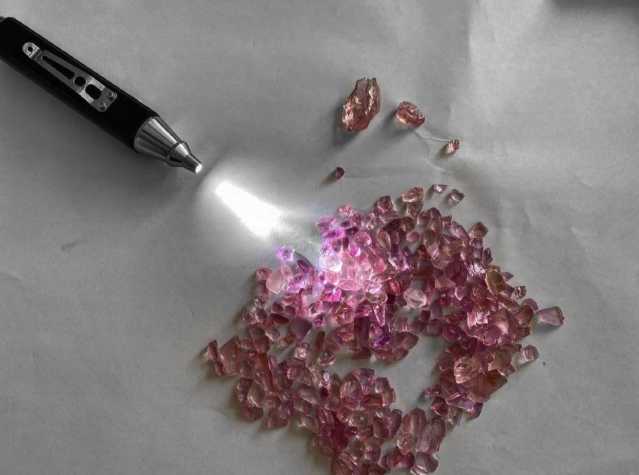 A parcel of pink spinel rough spread on white paper, lit from one side by a gemmological torch
